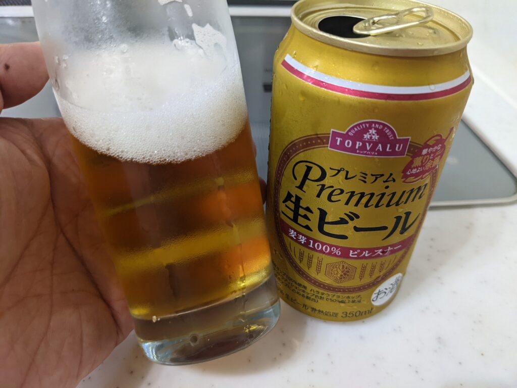 「トップバリュ」プレミアム生ビールが入ったグラスを傾けているところ