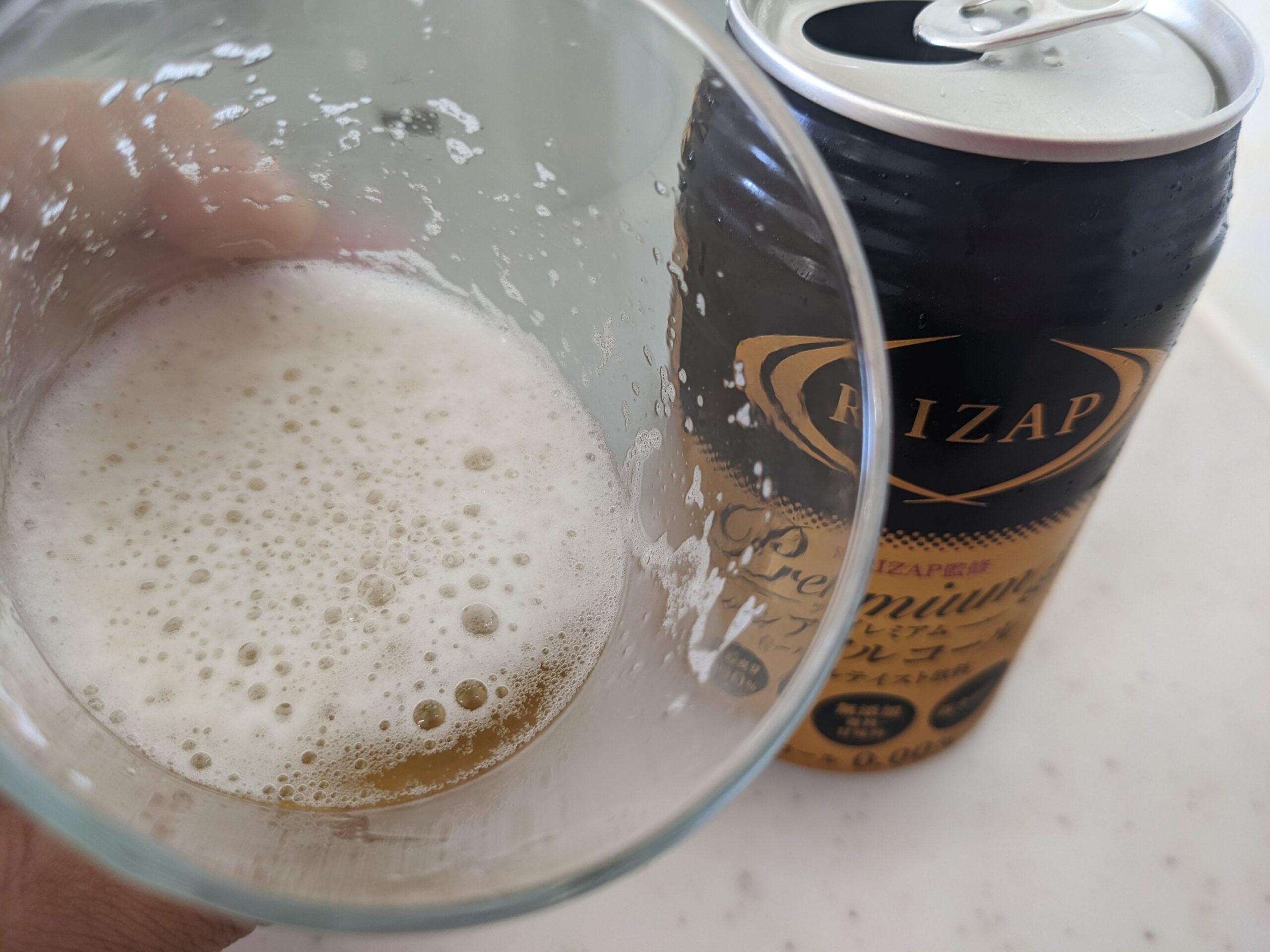 「RIZAP（ライザップ）プレミアムノンアルコールビールテイスト飲料」が入ったグラスを手前に傾けているところ